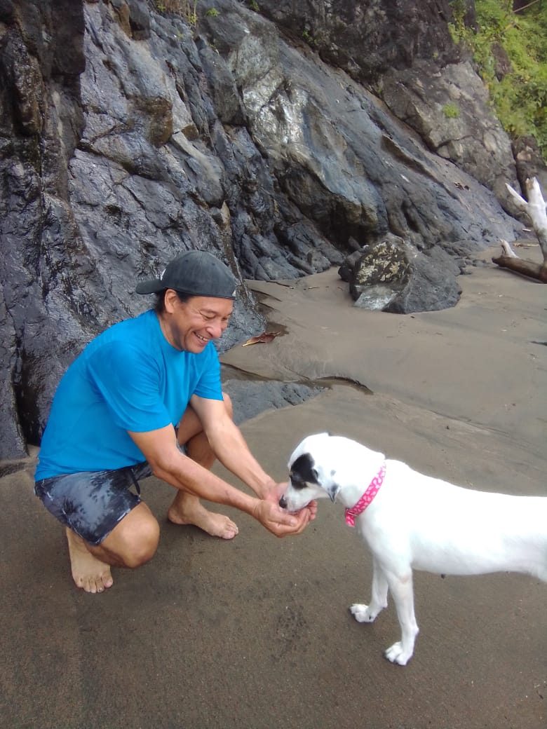 Nolberto feeding a white rescue dog on the beach